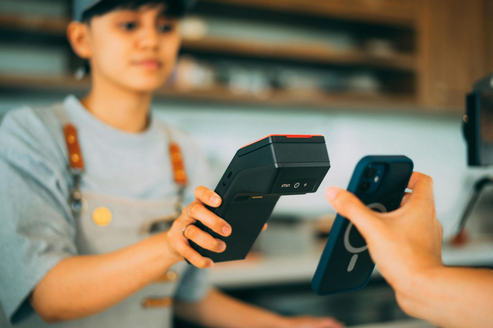 A cashier processes a contactless payment using a smartphone and card reader.