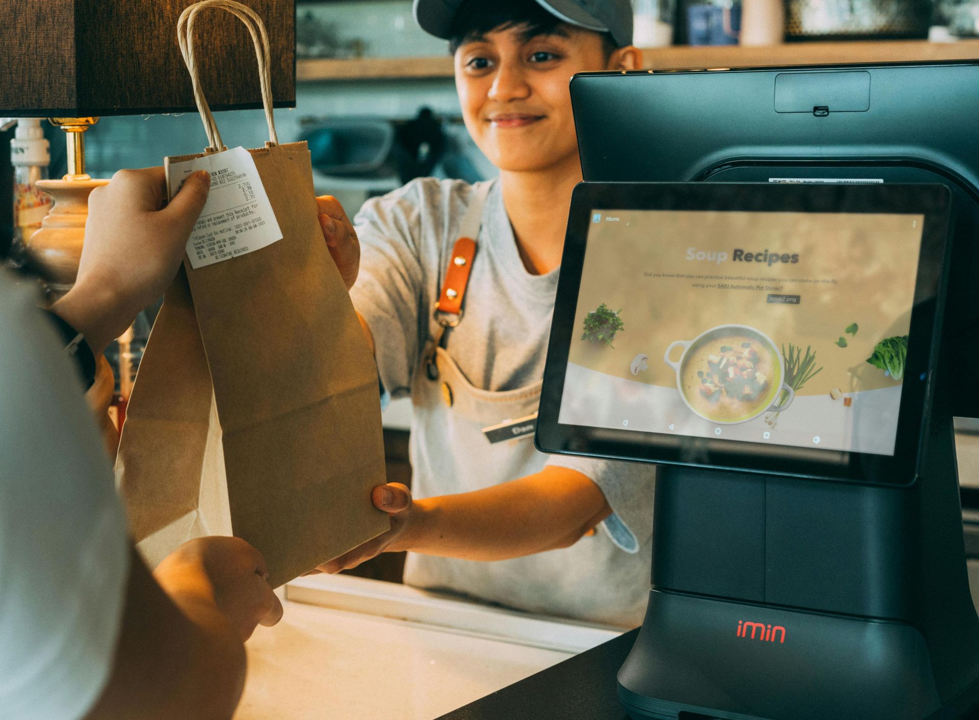 A smiling cashier hands a paper bag to a customer at a modern point of sale, showcasing customer service.